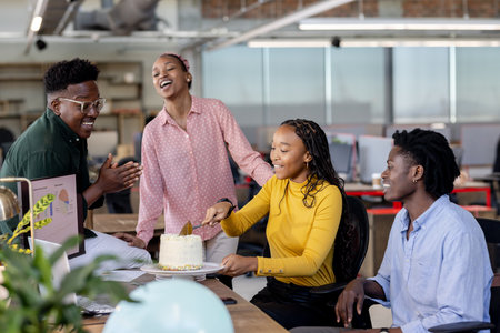 Celebrating birthday with cake, African American colleagues smiling in modern office. Celebration, office culture, teamwork, corporate, diversity, happinessの写真素材