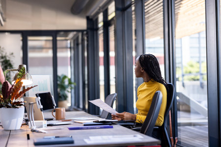 Businesswoman in yellow shirt reviewing documents at modern office desk. professional, analysis, commerce, management, corporate, executiveの写真素材