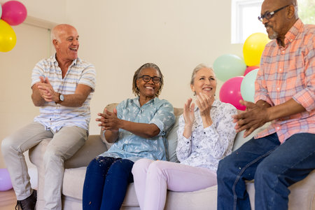 Senior friends clapping and laughing together on sofa at festive gathering. Celebration, friendship,...