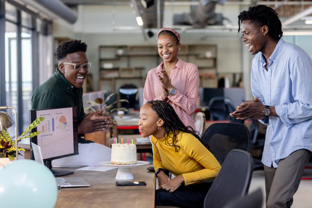 Colleagues celebrating birthday in office as woman blows out candles on cake. Celebration, party, teamwork, happiness, funの写真素材