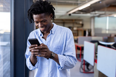 Smiling man using smartphone in modern office, enjoying productive workday. Technology, business,...