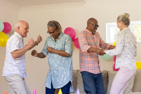 Senior friends dancing joyfully at home, celebrating with colorful balloons. Friendship, elderly, celebration, party, happiness, lifestyleの写真素材