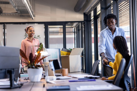 Greeting each other in modern office, African American colleagues smiling and collaborating. Collaboration, teamwork, corporate, diversity, professional, workplaceの写真素材