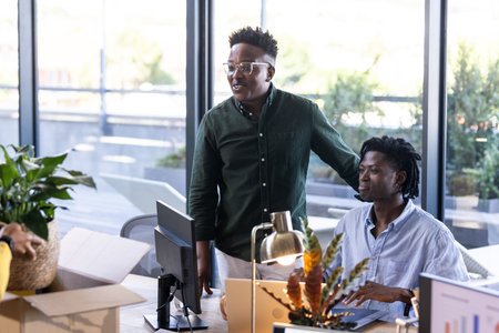 Collaborating at desk, African American colleagues discussing project ideas in modern office. Teamwork, brainstorming, diversity, collaboration, innovation, professionalsの写真素材
