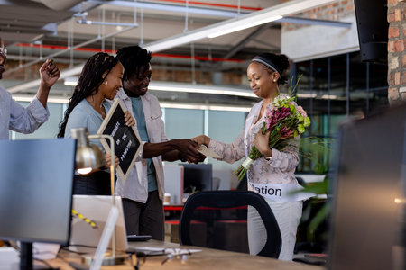 Celebrating promotion with flowers and handshake, African American colleagues in office. Business, teamwork, success, achievement, congratulations, diversityの写真素材