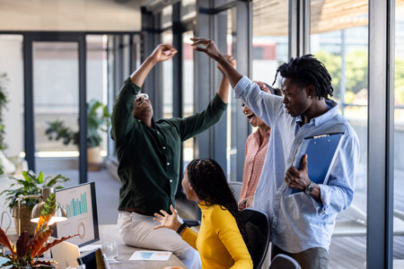 Team celebrating success in modern office, raising hands and smiling with joy. Teamwork, celebration, collaboration, achievement, diversity, motivationの写真素材