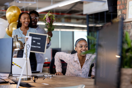 Surprising coworker with flowers and sign, colleagues celebrate promotion at office. Teamwork, congratulations, celebration, corporate, happiness, appreciationの写真素材