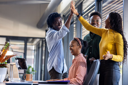 Team celebrating success in modern office, high-fiving with joyful expressions. Teamwork, celebration, achievement, victory, corporate, collaborationの写真素材