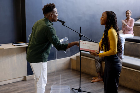 Receiving certificate on stage, young woman applauded by audience in modern office. Achievement, recognition, success, applause, businesswoman, corporateの写真素材