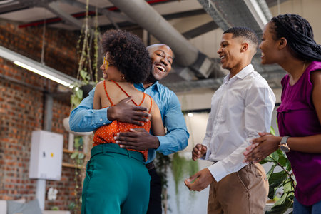 Colleagues celebrating success with joyful hugs and laughter in modern office. Teamwork,...