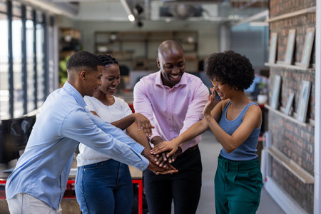 Diverse team in office celebrating success with hands together, smiling joyfully. Teamwork,...