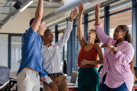 Diverse team celebrating success with high fives in modern office setting. Teamwork, collaboration,...
