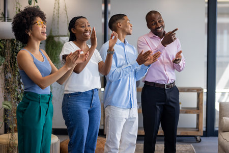 Clapping and smiling, African American colleagues celebrating in office, feeling joyful. Teamwork, celebration, collaboration, success, happiness, diversityの写真素材