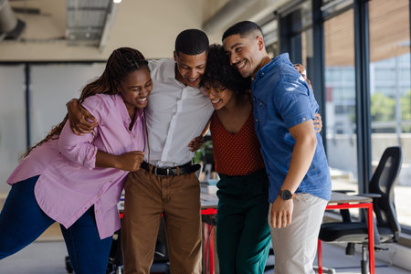 Diverse colleagues embracing and laughing together in modern office setting. Teamwork, collaboration, camaraderie, professional, corporate, friendshipの写真素材