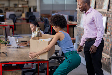 Moving office supplies, African American colleagues collaborating efficiently in modern workspace. Teamwork, diversity, collaboration, productivity, brainstorming, efficiencyの写真素材