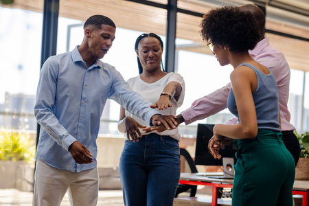 Celebrating teamwork, African American colleagues joining hands in office for success. unity,...