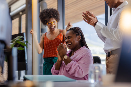 Colleagues celebrating success in office, African American woman smiling joyfully. Teamwork, celebration, corporate, diversity, achievement, businessの写真素材