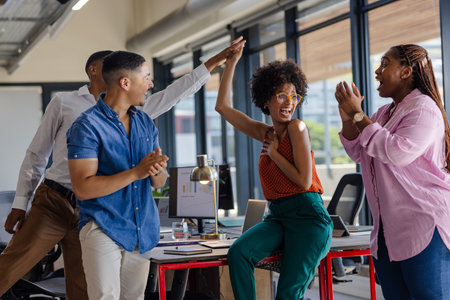 Colleagues celebrating success with high fives in modern office setting. Teamwork, collaboration,...