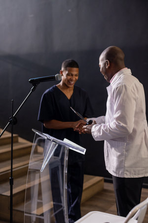 Man receiving award on stage, smiling and shaking hands with presenter. Achievement, recognition, ceremony, success, celebration, honorの写真素材