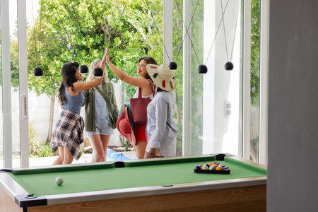 Women celebrating with high fives near pool table, enjoying leisure time together. friendship,...