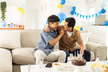 Two men laughing and celebrating birthday at home with cake and decorations. Celebration, party, friends, happiness, candles, joyfulの写真素材
