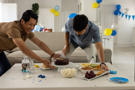 Men setting up birthday party table with cake, snacks, and decorations at home. Celebration, festive, table setting, desserts, gathering, cheerfulの写真素材