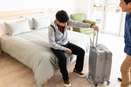 Man sitting on bed with suitcase, preparing for travel at home. preparation, packing, luggage, journey, vacation, adventureの写真素材