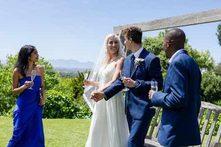 Bride and groom holding hands, celebrating with friends outdoors, enjoying champagne. Wedding, celebration, newlyweds, friendship, happiness, toastingの写真素材