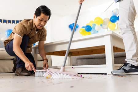 Father and son cleaning living room floor after birthday party celebration. Cleanup, family, bonding, chores, household, fatherhoodの写真素材