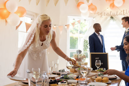 Bride arranging table setting at wedding reception with guests enjoying celebration. arrangement, party, venue, decoration, event, tablescapeの写真素材
