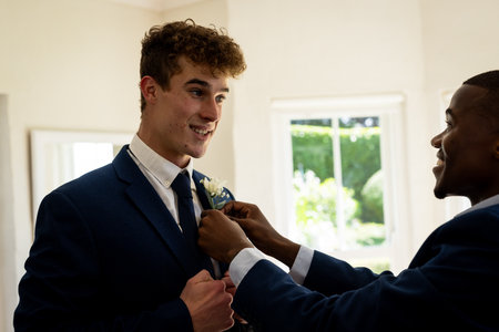 Groom smiling while friend adjusts boutonniere, preparing for wedding ceremony. preparation,...