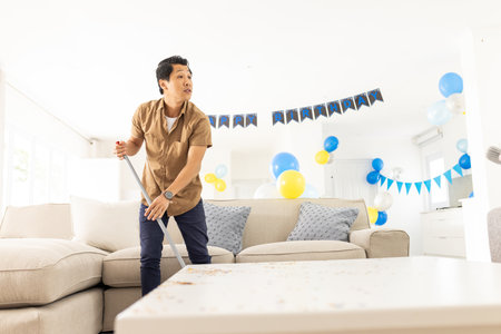 Cleaning living room, man sweeping floor with broom for celebration with balloons. Housekeeping, domestic, party, festive, chores, tidyの写真素材