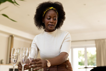 Woman setting table with champagne glasses at home, preparing for gathering. Celebration, dining, festive, preparation, luxury, hospitalityの写真素材