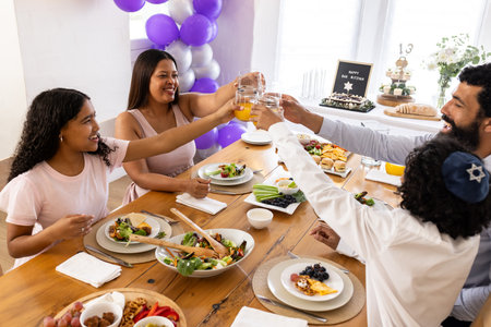 Family celebrating Bar Mitzvah at home, toasting with orange juice around table. Celebration, tradition, milestone, culture, gathering, ceremonyの写真素材