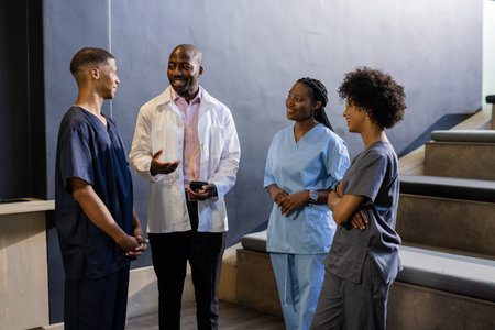 Discussing patient care, African American medical team smiling in hospital corridor. Healthcare, teamwork, collaboration, diversity, professionalism, doctorsの写真素材