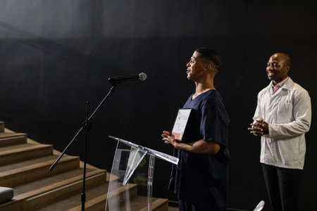 Receiving award on stage, African American man applauded by audience in auditorium. Achievement, ceremony, applause, recognition, success, winnerの写真素材