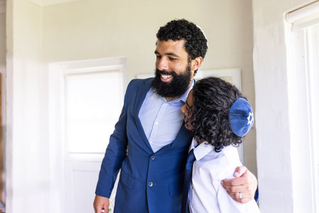 Father and son embracing joyfully during bar mitzvah at home. Family, tradition, happiness, bonding, love, culturalの写真素材