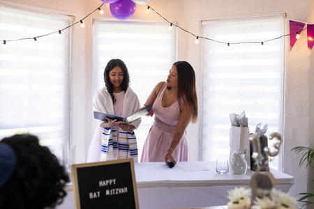 Young girl reading from book during Bat Mitzvah celebration with supportive woman. Religion, mentor, tradition, cultural, guidance, coming of ageの写真素材
