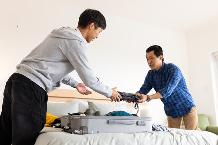 Father and son packing suitcase together on bed, preparing for travel adventure. Family, bonding, preparation, vacation, journey, leisureの写真素材