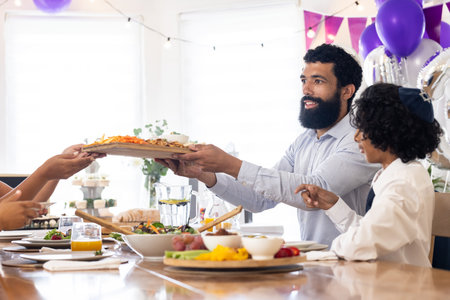 African American man serving food at festive table during family celebration. tradition, gathering, diversity, sharing, joyの写真素材
