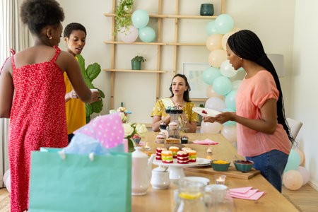 African American women enjoying tea party with desserts and decorations at home. Diversity, celebration, hospitality, friendship, bonding, gatheringの写真素材
