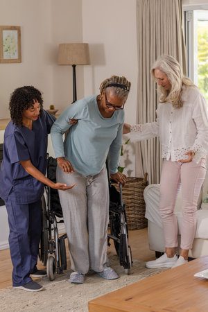 Caregiver and friend assisting senior woman standing from wheelchair at home. Caregiving, support, assistance, mobility, friendship, healthcareの写真素材