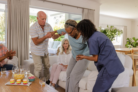 Senior friends helping each other stand up in cozy living room setting. Friendship, assistance, caregiving, companionship, togetherness, supportの写真素材