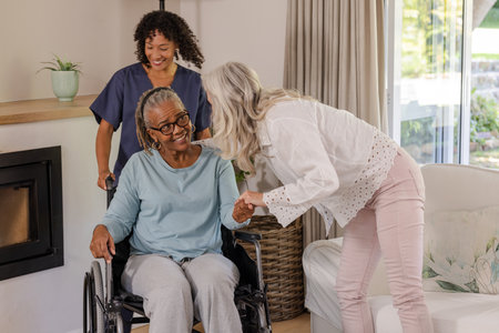 Caregiver assisting senior woman in wheelchair while friend visits at home. Elderly, support, companionship, assistance, disability, friendshipの写真素材