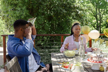 Friends enjoying outdoor birthday party with snacks and decorations on table. Celebration,...