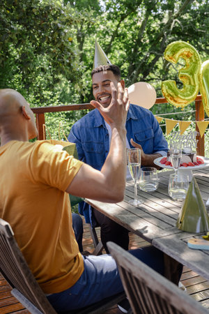 Friends celebrating birthday outdoors, wearing party hats and enjoying conversation. Celebration, friendship, socializing, happiness, gathering, leisureの写真素材