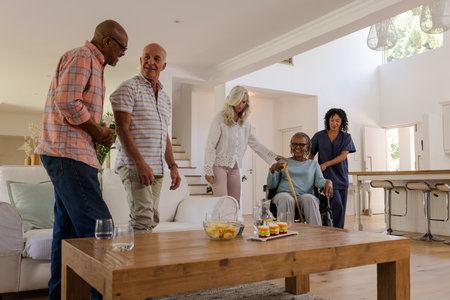 Senior friends enjoying conversation at home with caregiver assisting in wheelchair. Elderly,...