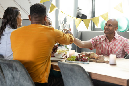 Friends toasting with drinks at dinner table, celebrating together indoors. Celebration, friendship, gathering, dining, beverages, partyの写真素材