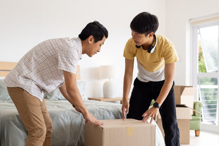 Father and son unpacking cardboard box together in bright bedroom. Family, bonding, moving, parenting, togetherness, lifestyleの写真素材