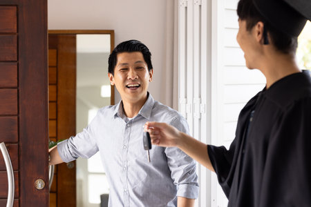 Father welcoming graduate son home, smiling as he receives car keys at door. Graduation, achievement, family, celebration, success, giftの写真素材